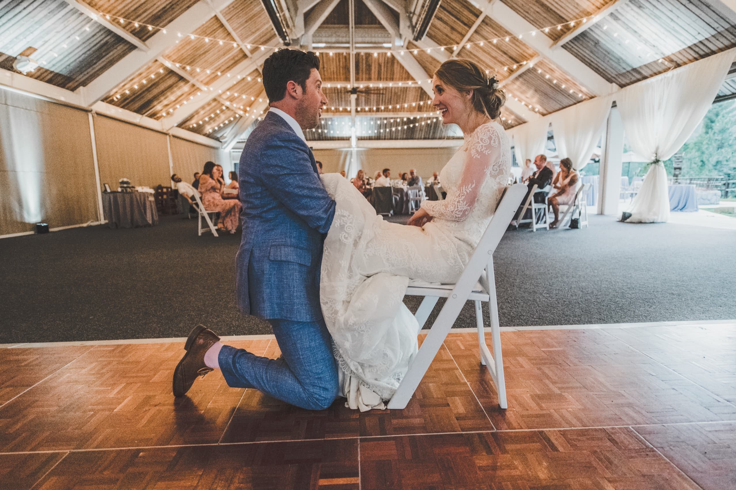 Billy kneels laughing at Jolly during the dance floor reception under string lights at the Tenaya pavilion