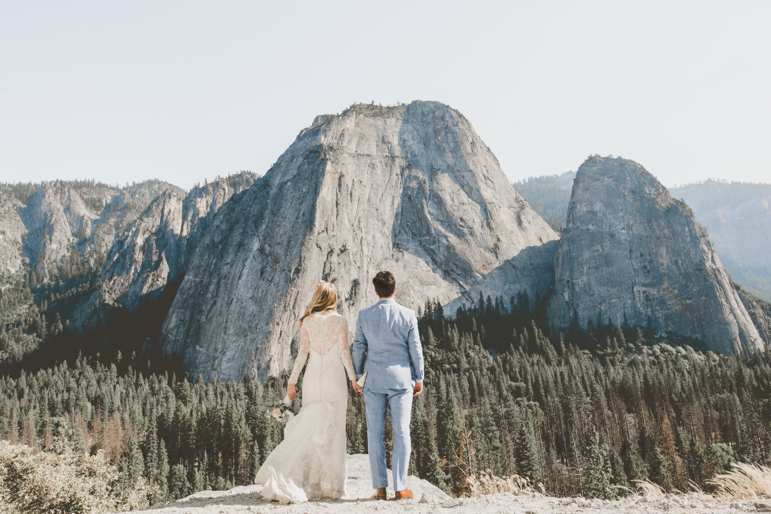 Jolly and Billy from behind hand in hand looking out at Yosemite granite domes and pine forest