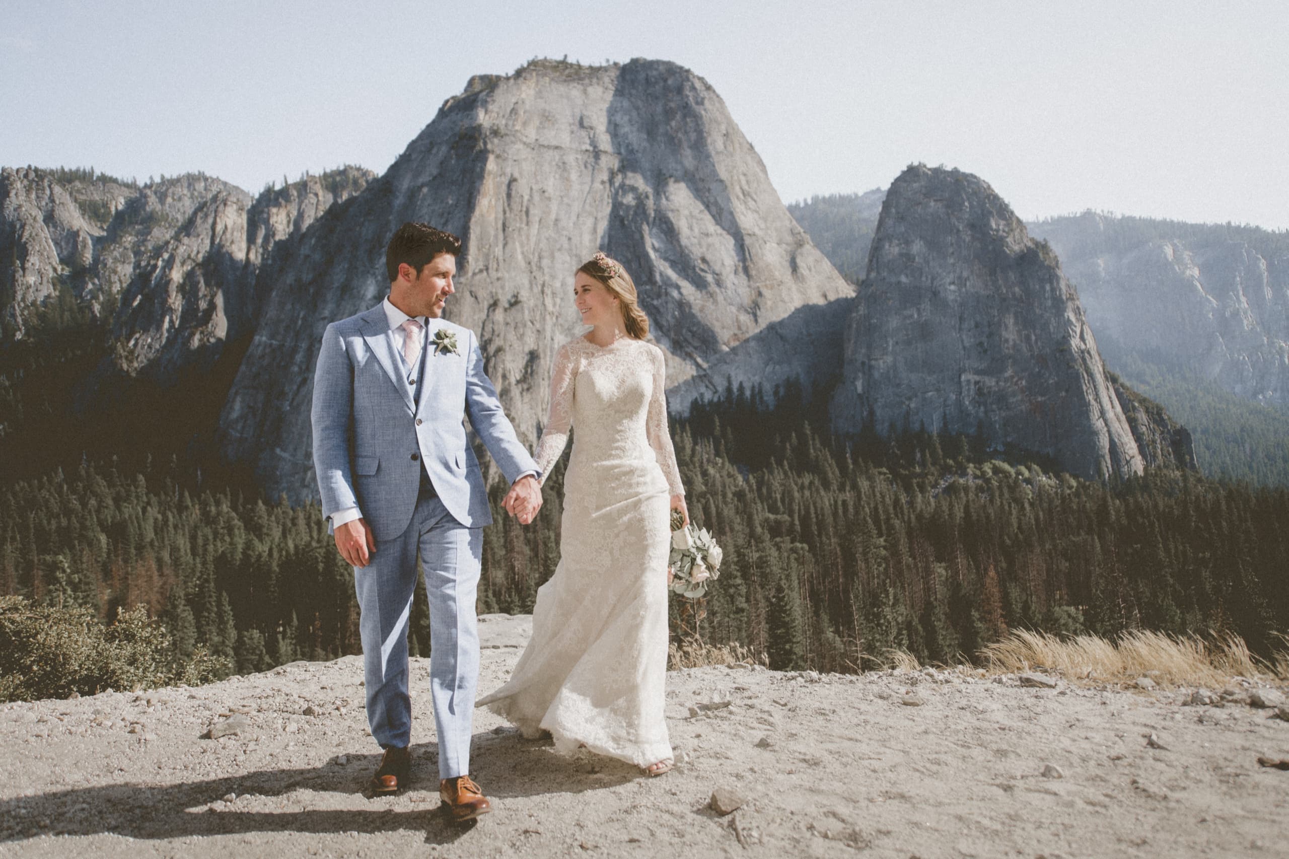 Jolly and Billy walking hand in hand smiling at each other with Yosemite granite peaks behind them