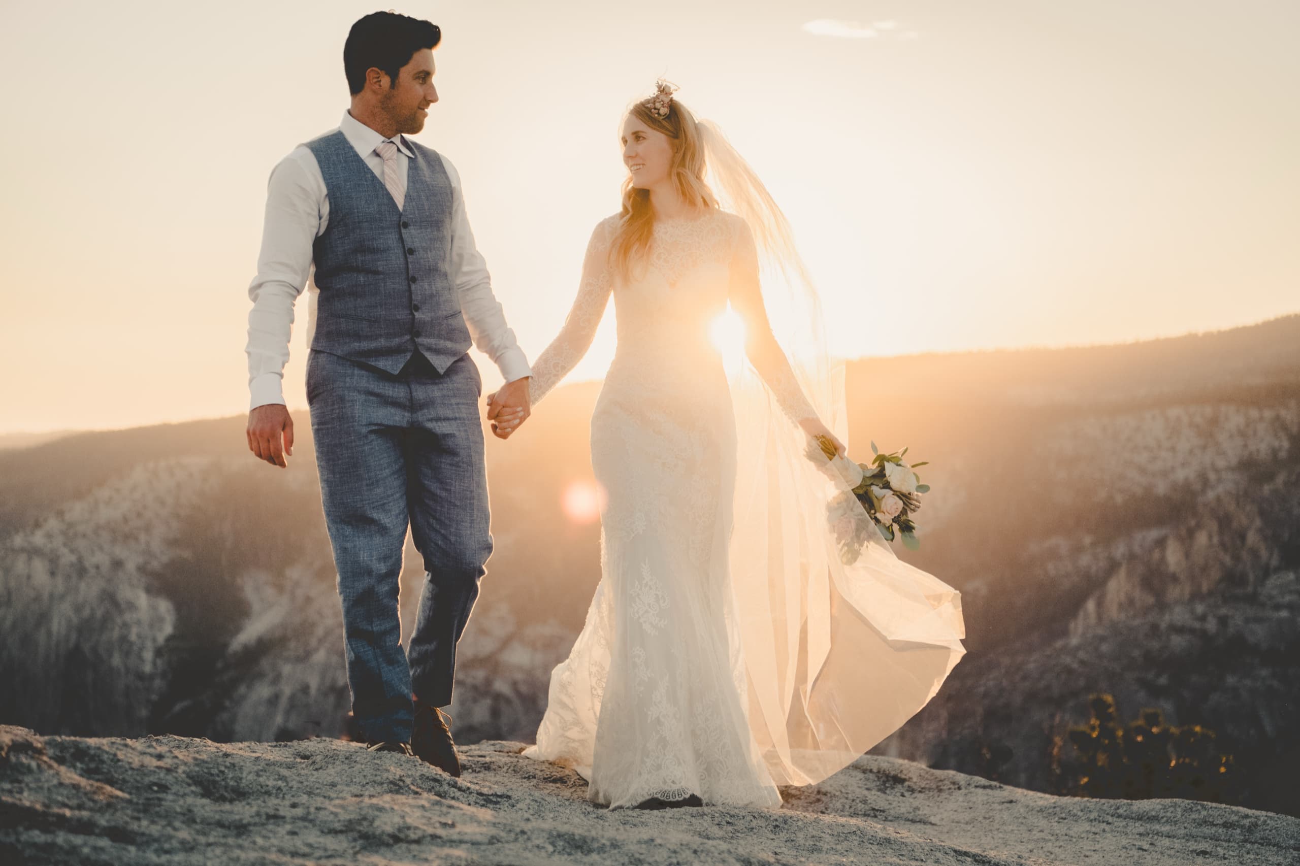 Jolly and Billy walking hand in hand on a granite ridge with sun flare at golden hour