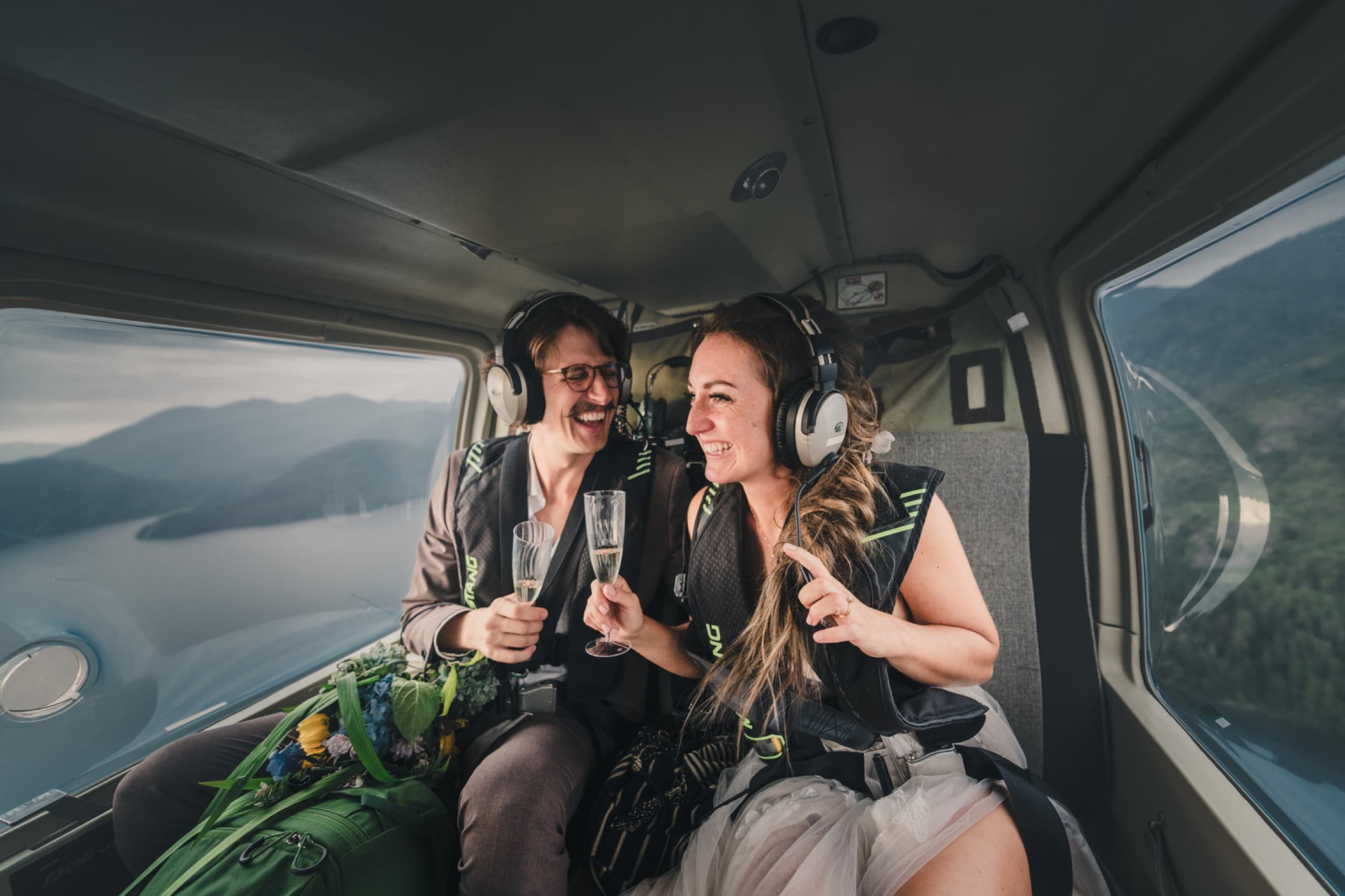 Couple in headsets laughing on a helicopter flight into the mountains